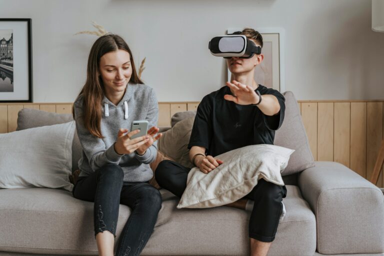 A woman with a smartphone and a man using VR headset on a cozy sofa, exploring technology indoors.